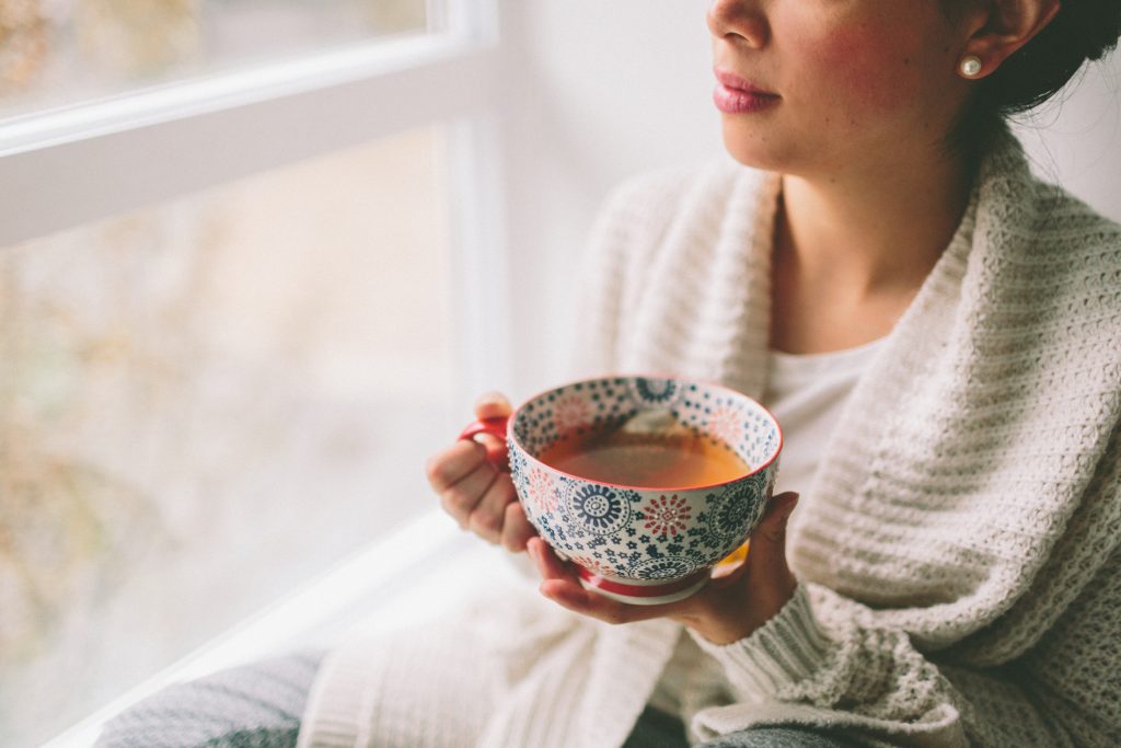 Women holding hot liquid by window